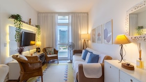 Ein modernes Hotelzimmer mit Flachbildfernseher, einer Couch, einem Esstisch und einem großen Fenster mit Vorhängen.