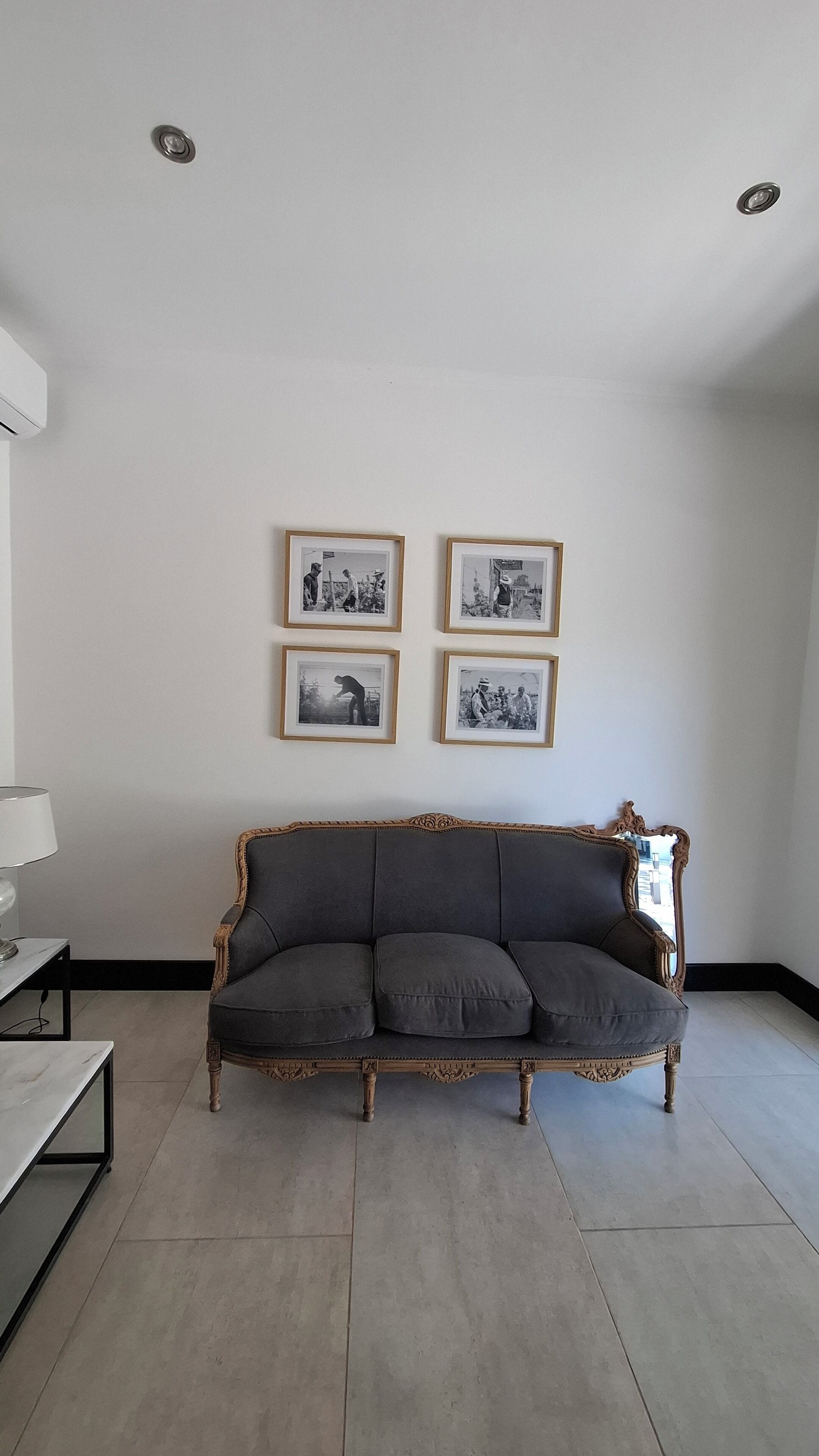 A living room with a dark grey upholstered sofa, a marble coffee table, and a white wall with four black and white framed photographs.