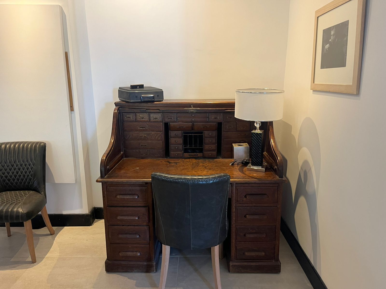 Un bureau en bois avec des tiroirs, une chaise, une lampe et un tableau encadré accroché au mur.