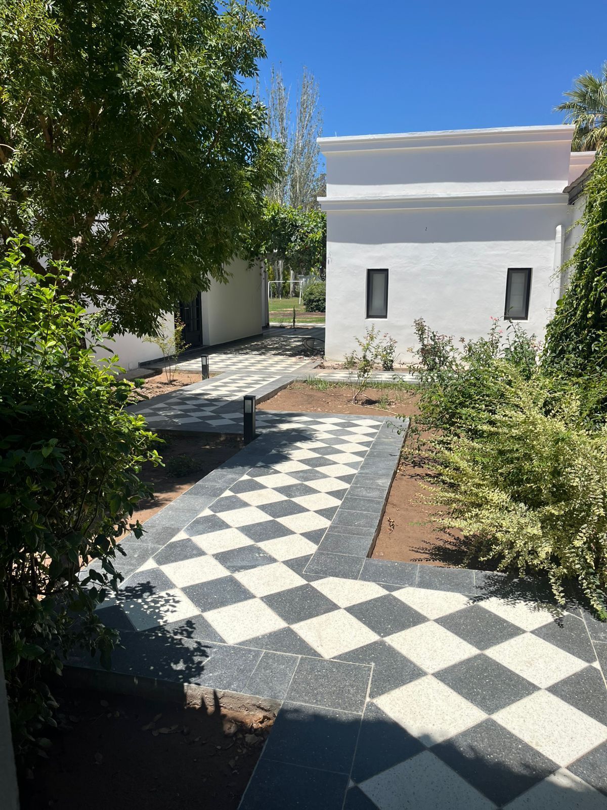 Une cour avec un chemin pavé de carreaux aux motifs géométriques, entourée de verdure et de bâtiments blancs.