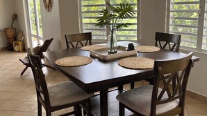 A dining area with a large wooden table, six chairs, and a central plant. - 3-bedroom house with Solar Energy, Water cistern, AC, and high speed internet. (Canaboncito)
