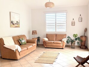 A living room with two sofas, a woven rug, a wooden bench, and a window with blinds.