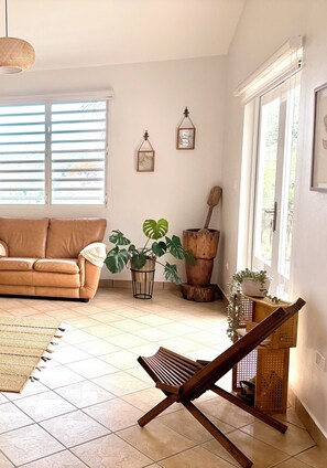 Una sala de estar con un sofá, una silla de madera y plantas en macetas.