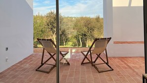 A room with a large sliding glass door leading to an outdoor patio with two wooden chairs and a small table. - CASA DO REGADIO - HOUSE 2, A country and sea retreat on the Alentejo coast,  (Zambujeira do Mar)