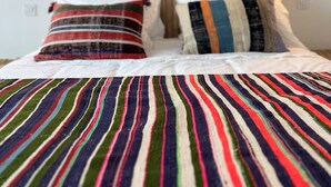 A bed with a striped blanket, two pillows with multicolored stripes, and a wooden headboard. - CASA DO REGADIO - HOUSE 2, A country and sea retreat on the Alentejo coast,  (Zambujeira do Mar)