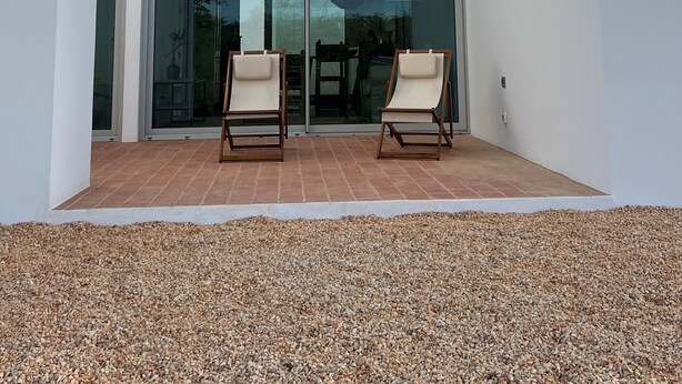 A modern house with a patio area featuring two chairs and a glass door leading to an interior space. - CASA DO REGADIO - HOUSE 2, A country and sea retreat on the Alentejo coast,  (Zambujeira do Mar)