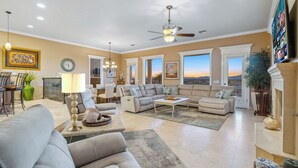 A spacious living room with a large sofa, a coffee table, and a fireplace. There are multiple windows offering a view of the outdoors. - Paradise Riverfront Home with Spa and Dock Sleeps 16+ (Bullhead City)