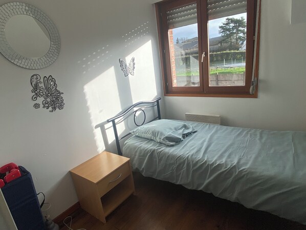 A bedroom with a single bed, a wooden nightstand, a mirror, and a window with blinds.