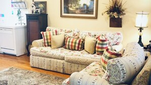 Una sala de estar con un sofá modular, alfombra, un cuadro enmarcado, un aparador y una lámpara.