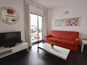 Una sala moderna con un televisor de pantalla plana, un sofá rojo, una mesa de centro blanca y un balcón con vistas.