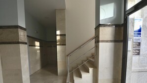 Un pasillo con piso de mármol, una escalera metálica y una puerta de cristal con señalización.