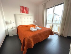 Habitación de hotel con una cama grande, cabecera blanca, ventana con vistas a edificios y un cuadro abstracto rojo en la pared.