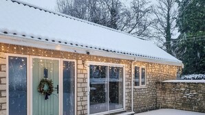A stone building with a snow-covered roof and a green door, featuring a wreath and string lights.