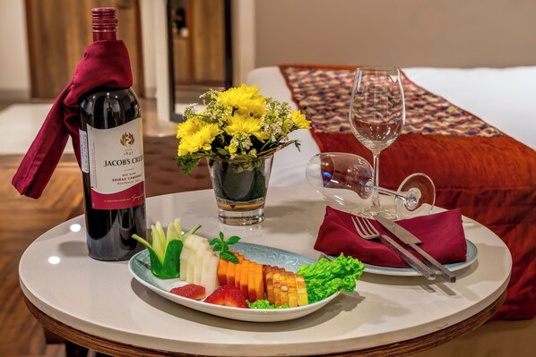 A dining table with a bottle of Jacob's Creek Shiraz, a glass of wine, a glass of water, a plate of fruit, and a vase of yellow flowers. - Comfort Inn Alstonia Amritsar (Amritsar)
