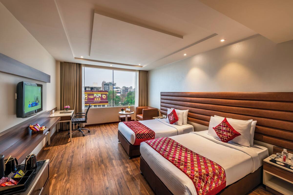 A hotel room with two beds, a desk, a TV, and a city view.