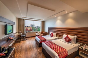 Ein Hotelzimmer mit zwei Betten, einem Schreibtisch, einem Fernseher und Blick auf die Stadt.