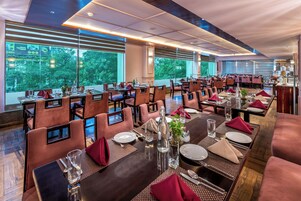 Un restaurante con varias mesas dispuestas para comer, amplios ventanales con vistas a árboles y una decoración interior moderna.