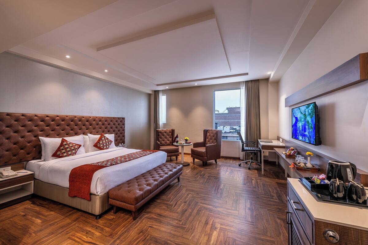 A modern hotel room with a large bed, a desk, a television, and a view of the city.