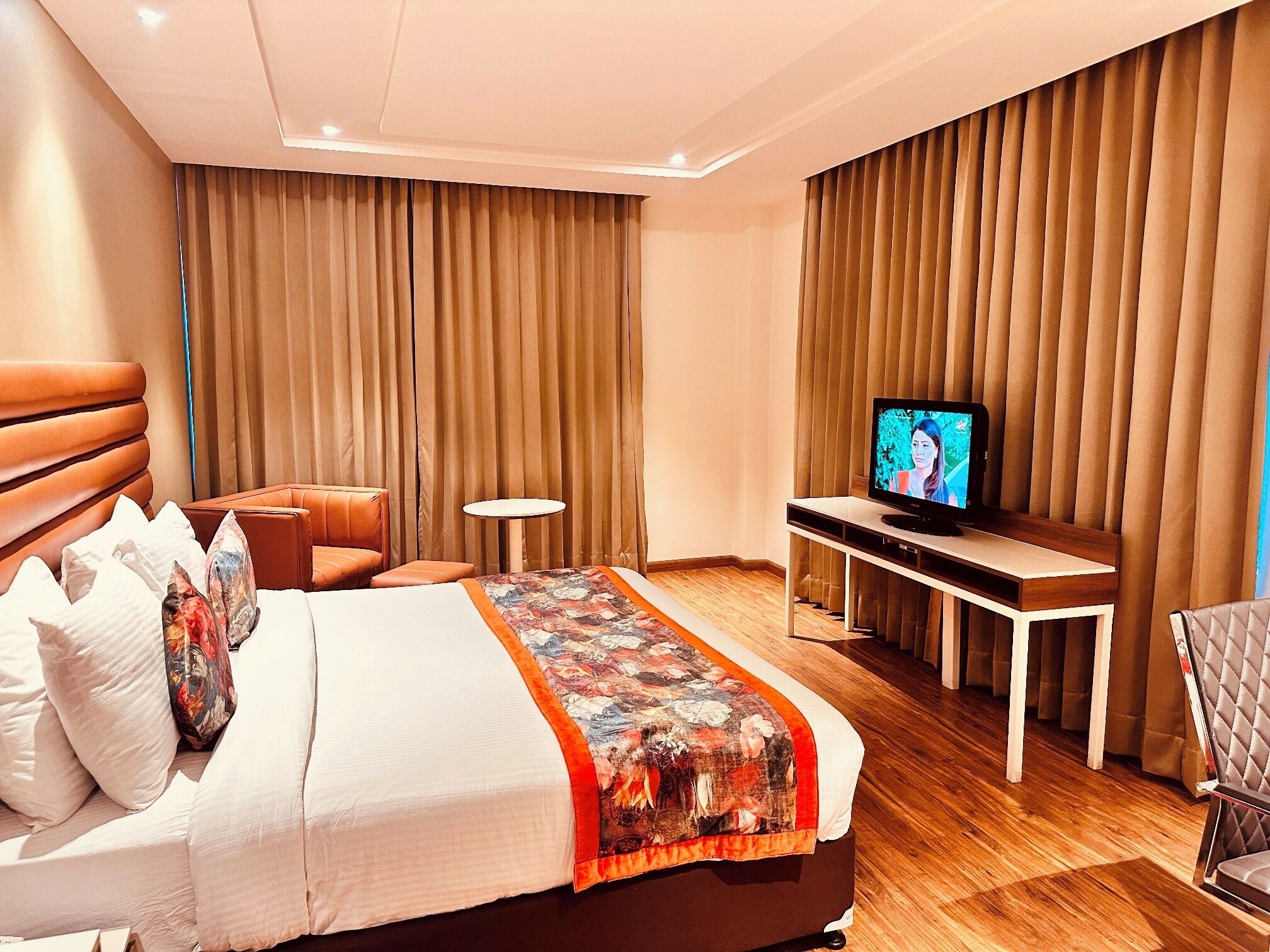 Quarto de hotel com cama, televisão, mesinha e uma cadeira.