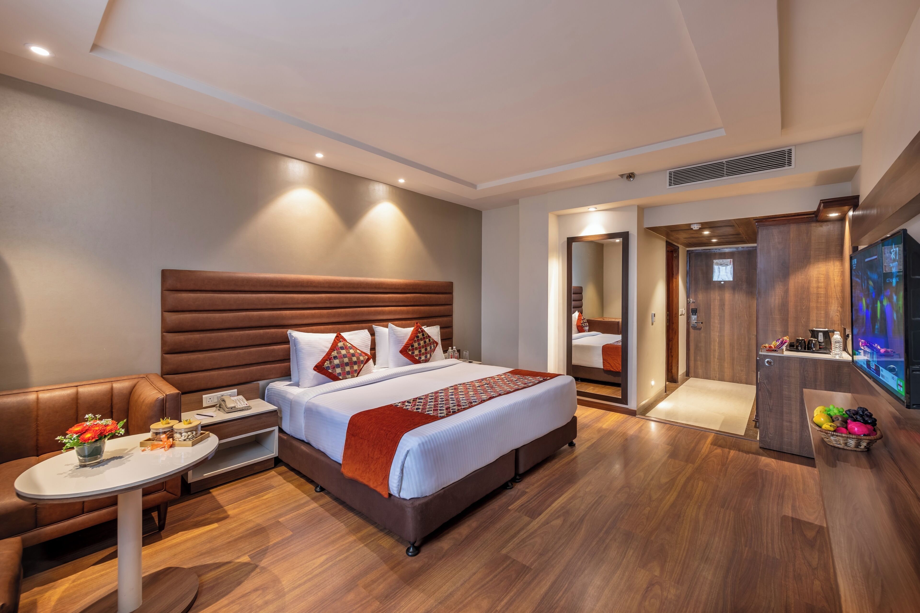 A modern hotel room with a large bed, a seating area, a small table, and a television.
