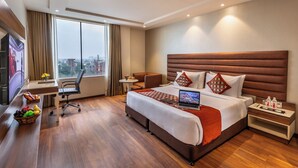 Una habitación de hotel moderna con una cama grande, un escritorio con una computadora portátil, un televisor y vistas a la ciudad.