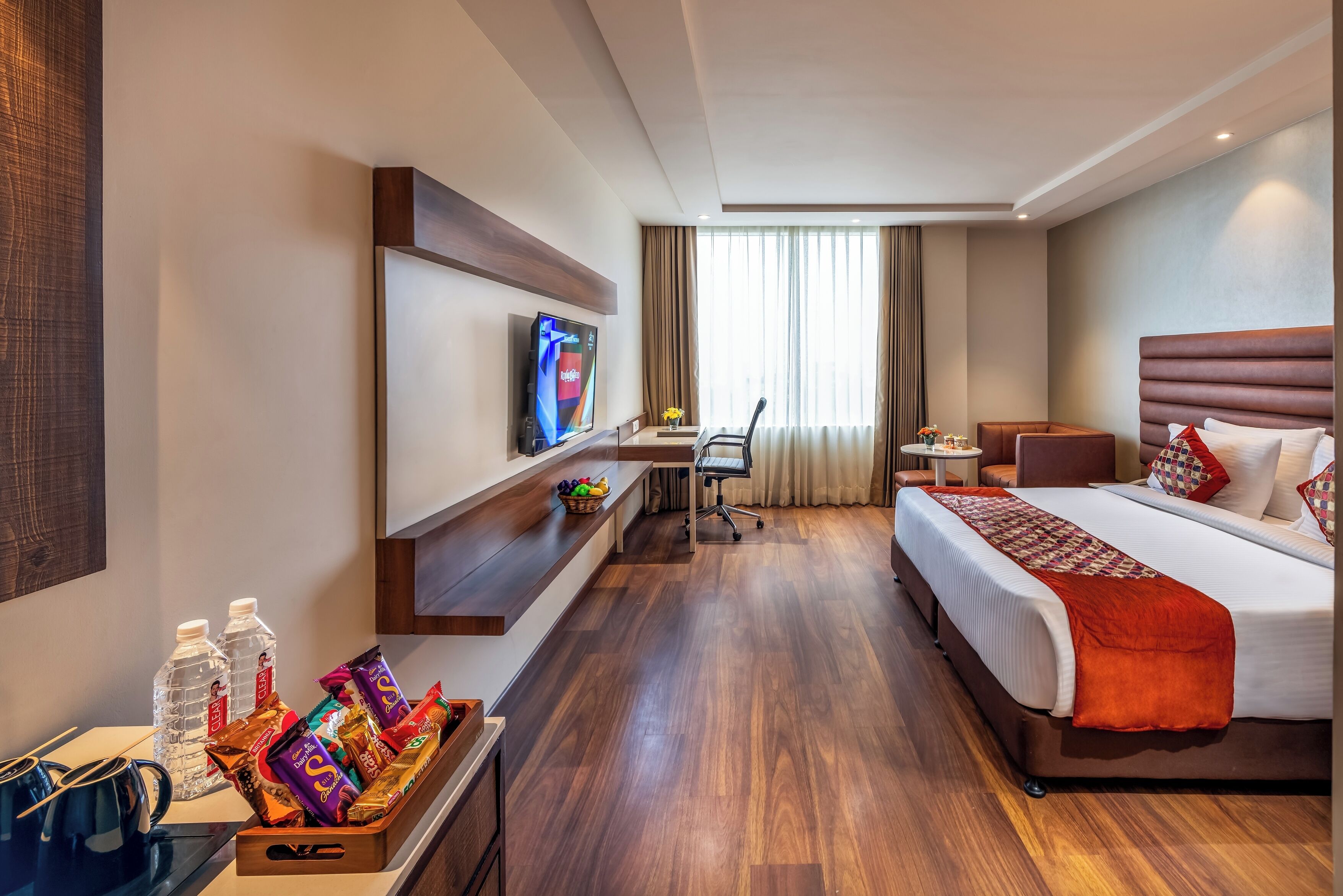 Habitación de hotel con cama, escritorio, televisor, una silla y una pequeña mesa con un florero.