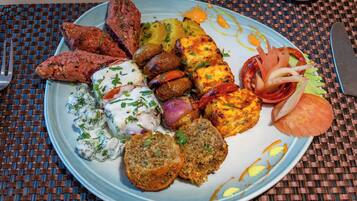 Un plato de comida con varias opciones, incluyendo verduras a la parrilla, un trozo de carne y un panecillo.