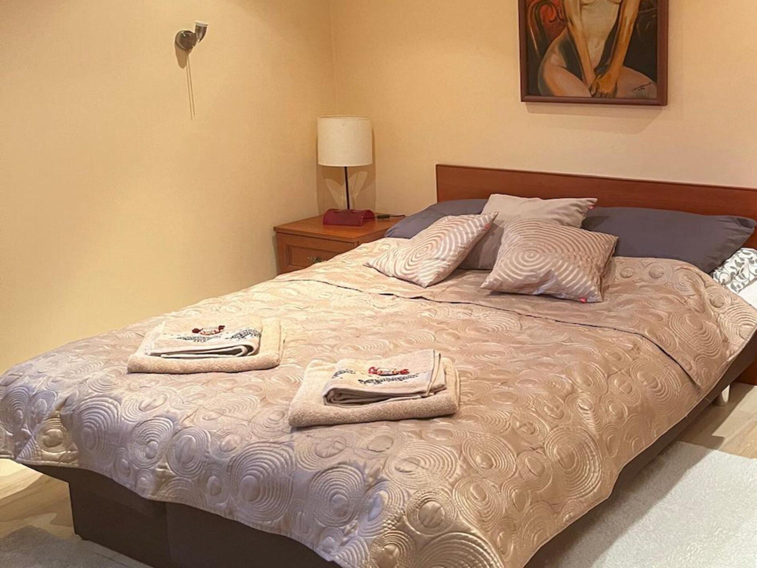 Una cama bien hecha con una colcha estampada, dos almohadas y dos toallas dobladas sobre la cama.