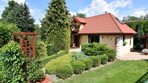 Una casa con tetto in tegole rosse, un giardino con siepi curate e un pergolato in legno.