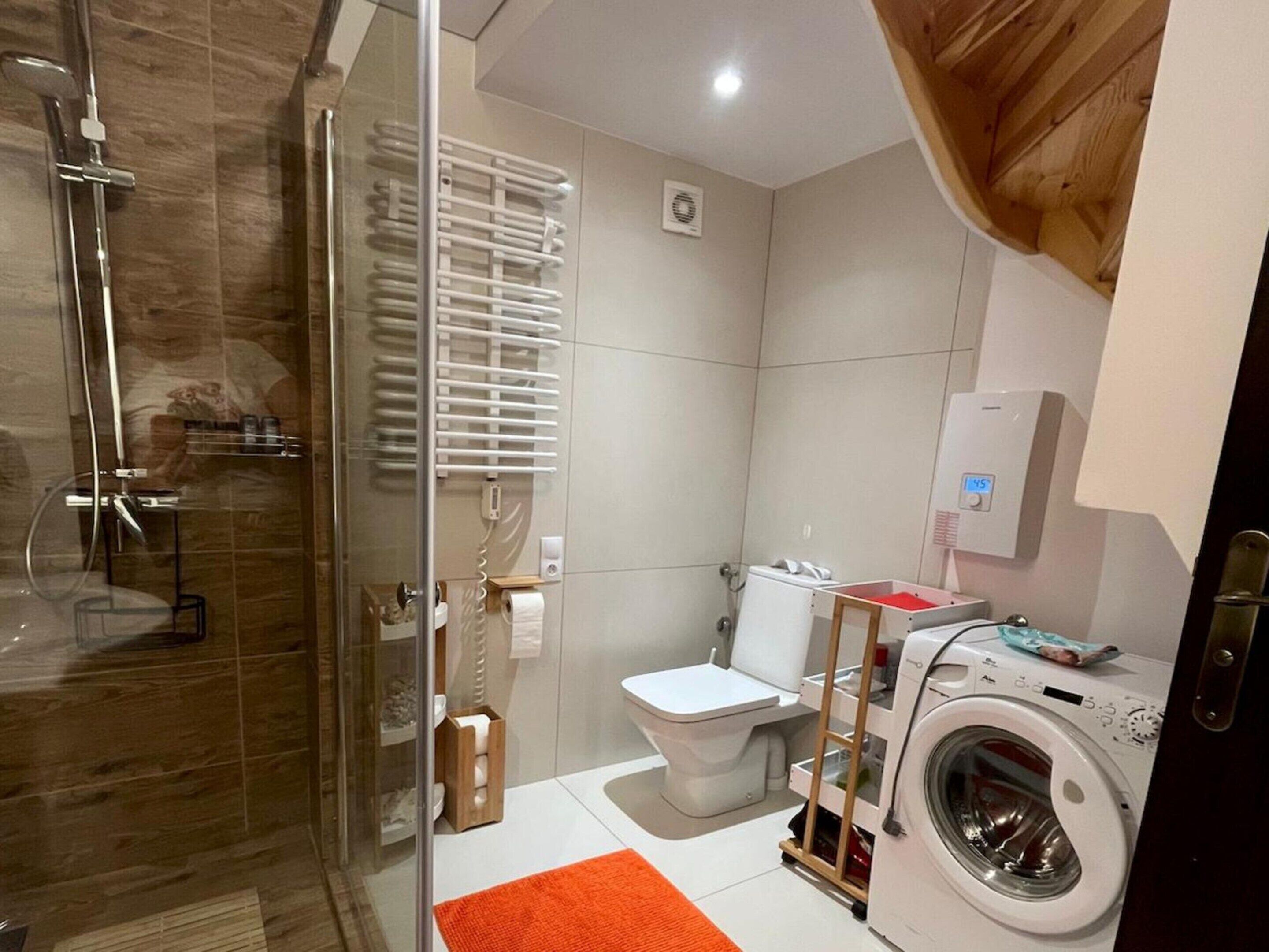 A modern bathroom with a glass shower enclosure, a toilet, a washing machine, and a towel rack.