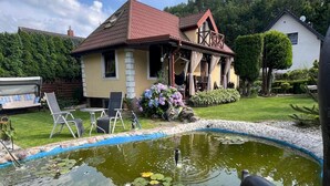Una casa con piscina circondata da un giardino, un patio con mobili da esterno e una piccola terrazza.