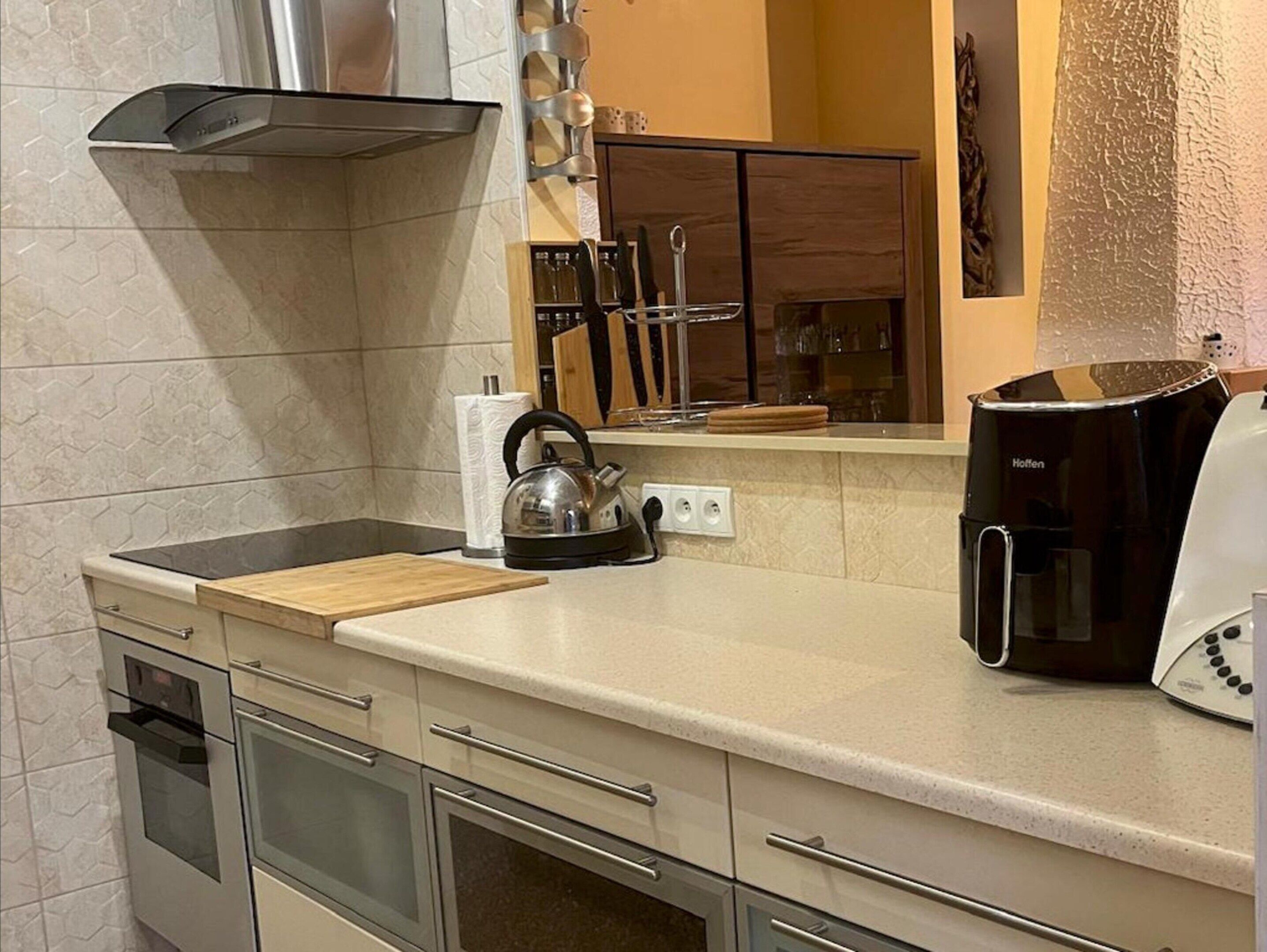 Una cucina moderna con cappa in acciaio inossidabile, bollitore, macchina da caffè e tagliere in legno.