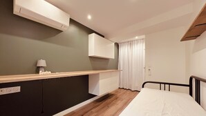 Une chambre moderne avec un lit, une table de chevet avec une lampe, un climatiseur fixé au mur et une fenêtre avec des rideaux.