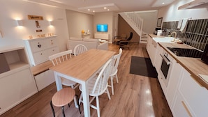Une cuisine moderne avec des meubles blancs, une table à manger en bois et un escalier menant à un autre niveau.
