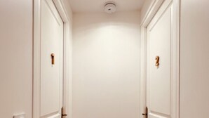 Un couloir étroit avec des portes blanches, un plancher en bois et un luminaire au plafond.