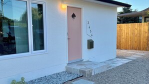 Ein modernes Haus mit weißer Fassade, einer rosafarbenen Tür und einem kleinen Garten mit Kies und trittfesten Pflastersteinen.