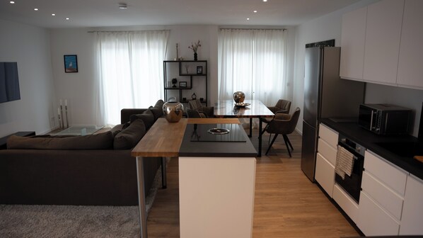 A modern living room with a sofa, a dining table, and a kitchen area with a refrigerator and microwave. - A quiet, tastefully furnished apartment located in the city center. (Rheinbach)