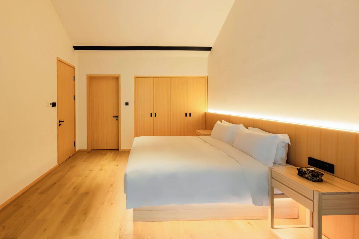 Quarto moderno com cama grande, guarda-roupa de madeira e mesa de cabeceira.