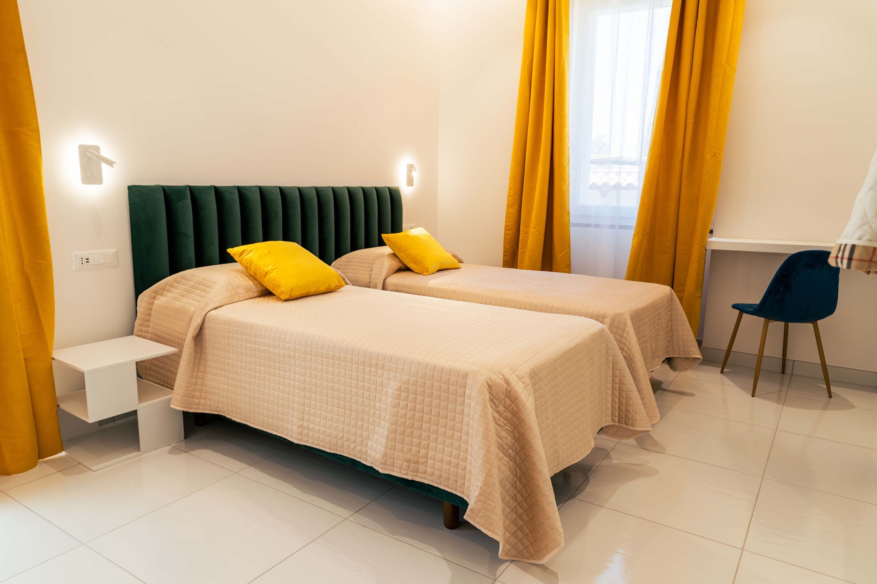 Una cama doble con cabecera verde, dos almohadas amarillas y una mesita de noche.