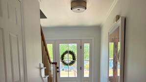 A hallway with a wooden floor, white walls, a door with a doorknob, a staircase with a wooden handrail, and a ceiling light fixture. - The Retreat at Bethany Beach Cove (Sussex County)
