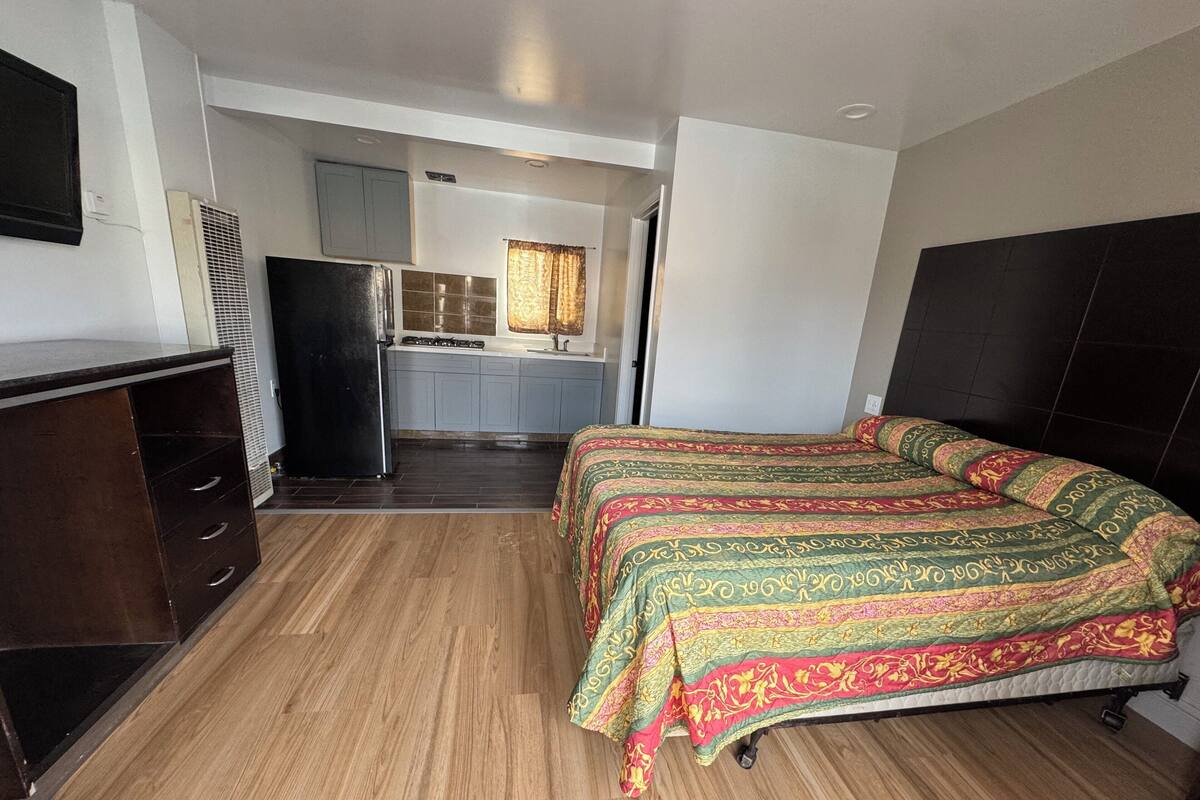 A compact room with a bed, a small kitchenette, and a wooden floor.