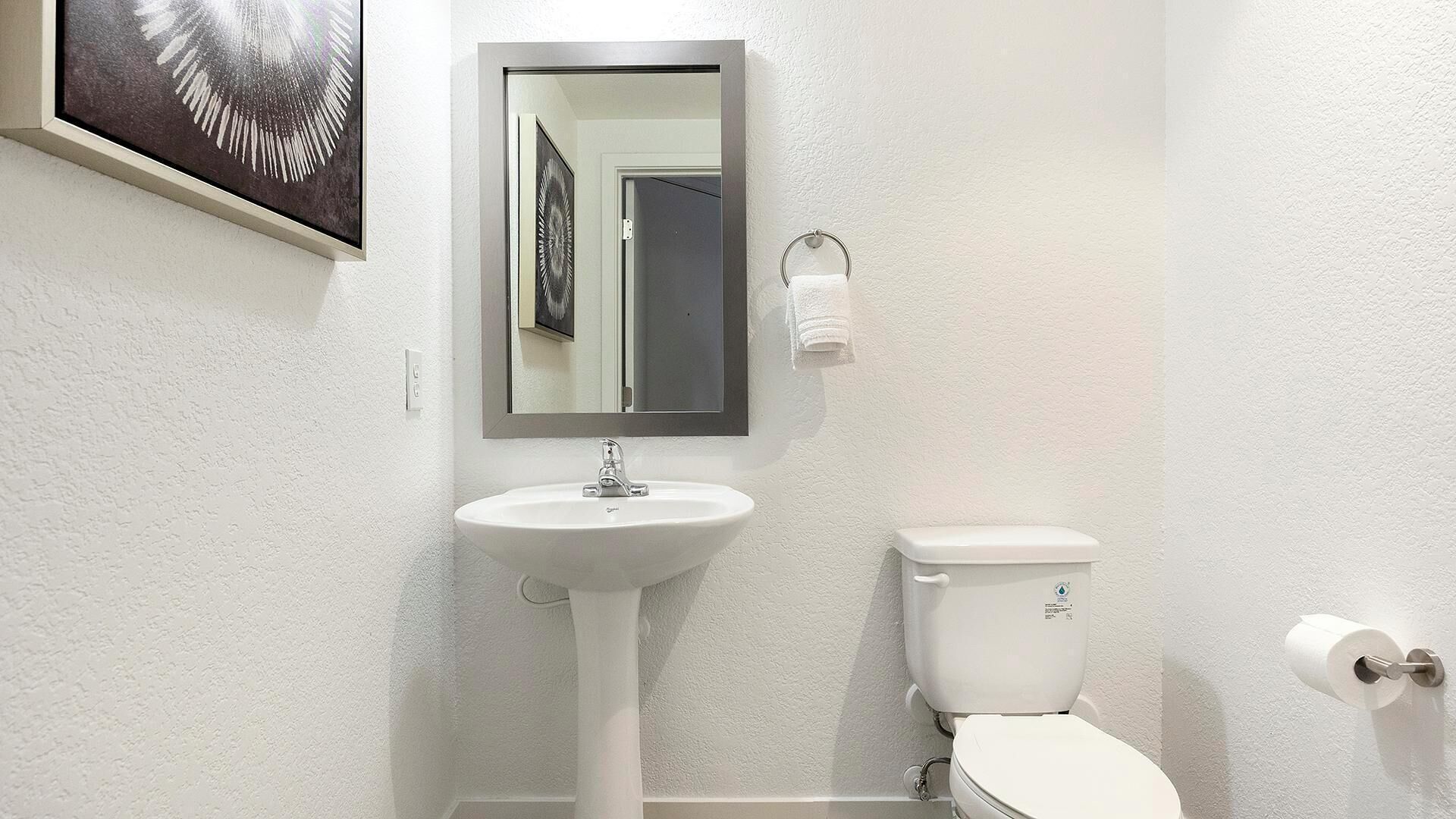 A bathroom with a white sink, a toilet, a mirror, and a framed picture on the wall.