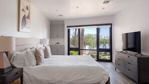 A bedroom with a bed, a TV, a dresser, and a view of palm trees. - Landing | Incredible Studio, Game Room, Gym (Tempe)