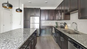 A modern kitchen with granite countertops, stainless steel appliances, and dark wood cabinets. - Landing | Stunning 1BD, Clubhouse, Yoga Studio (Fort Worth)