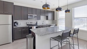 A modern kitchen with dark cabinets, stainless appliances, a granite countertop, and a bar area with stools. - Landing | Chic 1BD, Courtyard, Gym (Fort Worth)