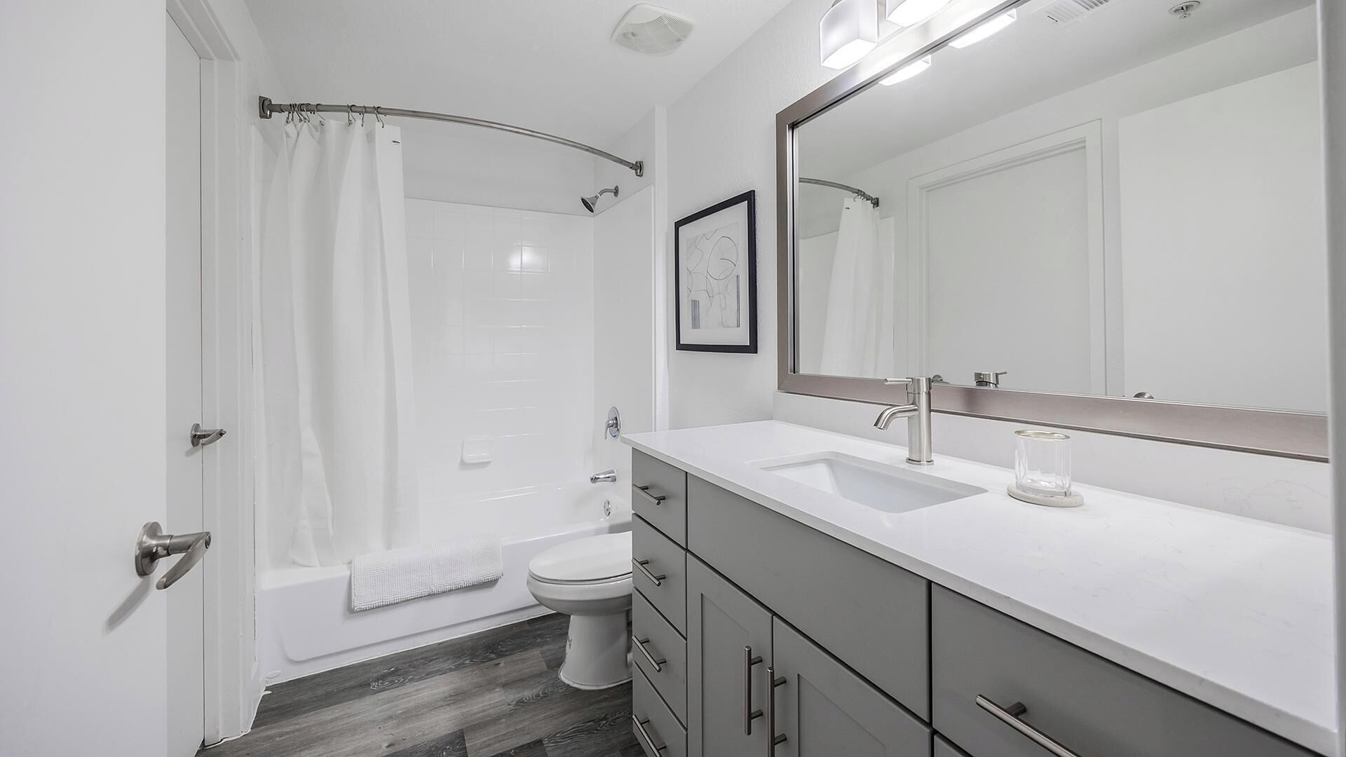 A modern bathroom with a bathtub, toilet, and vanity with a large mirror.