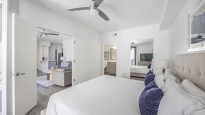 Une chambre d’hôtel moderne dotée d’un grand lit, d’un ventilateur de plafond, d’un bureau avec une lampe et d’une salle de bain visible à travers une porte ouverte.