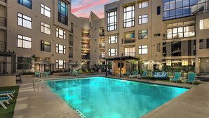 Un hôtel moderne doté d’une piscine centrale, d’un espace extérieur aménagé et d’un bâtiment à plusieurs étages avec des balcons.