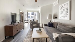 A modern living room with a flat-screen TV, a sofa, a coffee table, and a dining area with a chair and table. - Landing | Modern 2BD, Clubhouse, Yoga Studio (Tempe)