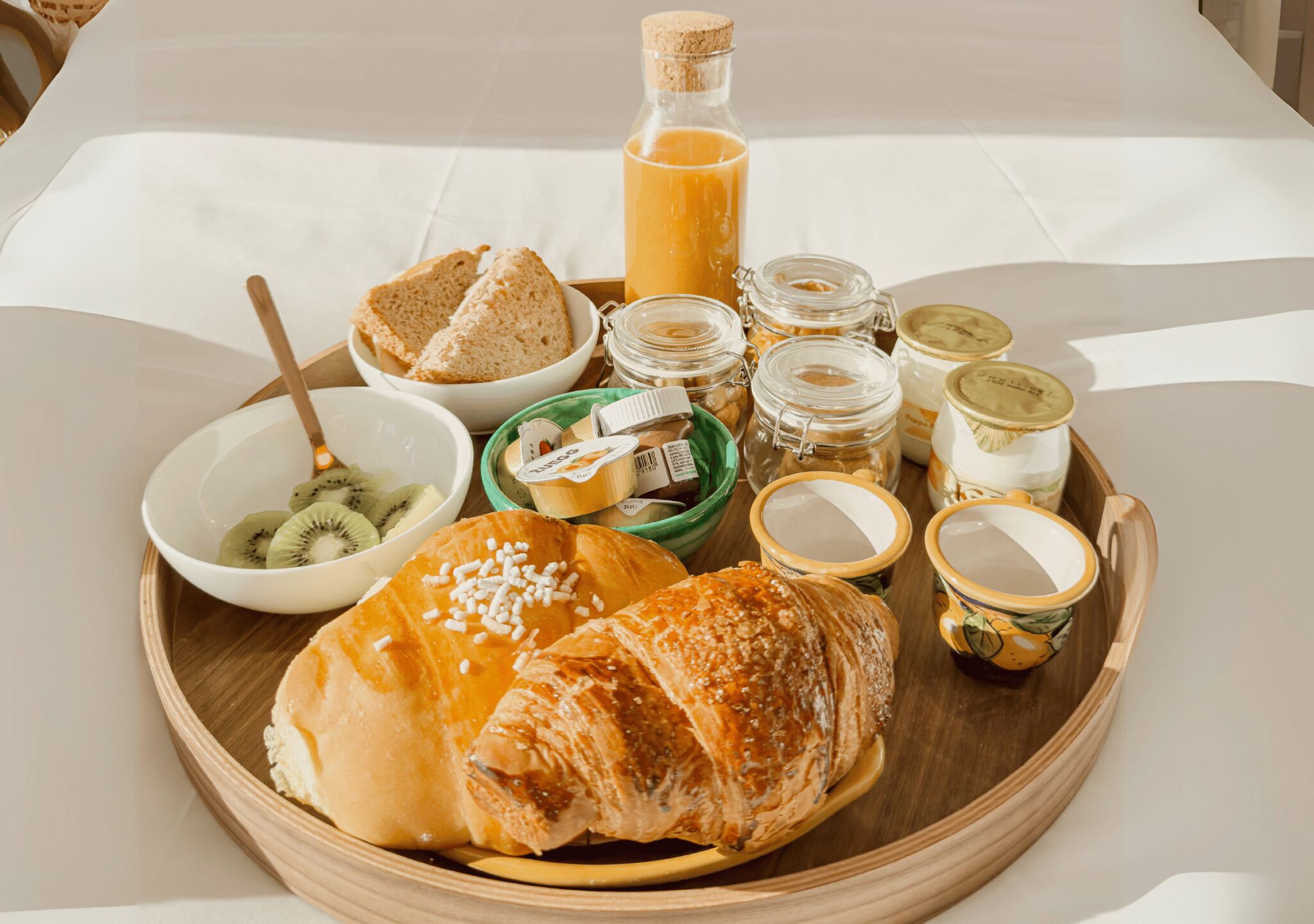 Bandeja de café da manhã com croissants, pão, fatias de kiwi e diversos acompanhamentos.